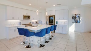 A modern kitchen with white cabinetry, a central island with bar stools, stainless steel appliances, and pendant lighting. - 2 Mi to Fantasy Springs Casino: Lakefront Retreat! (Indio)
