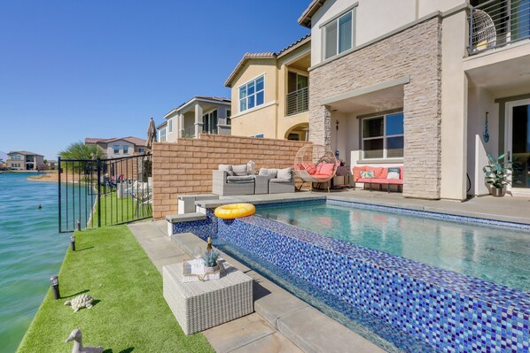 A swimming pool with a mosaic tile edge, surrounded by a brick wall and a patio area with outdoor furniture.