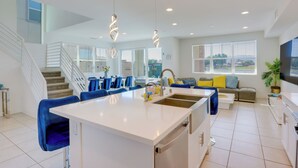 A modern kitchen with a central island, white cabinetry, and blue bar stools. - 2 Mi to Fantasy Springs Casino: Lakefront Retreat! (Indio)