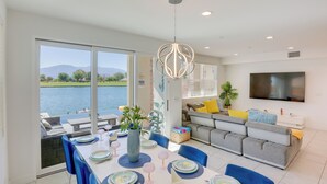 A modern living room with a large TV, grey sofa, and a dining area with blue chairs and a table set for six. - 2 Mi to Fantasy Springs Casino: Lakefront Retreat! (Indio)