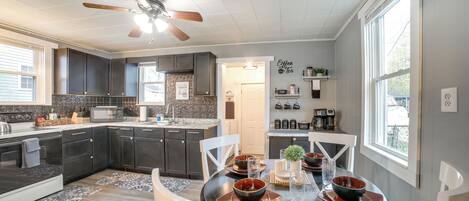 A modern kitchen with dark cabinets, a dining area with a round table, and a ceiling fan.