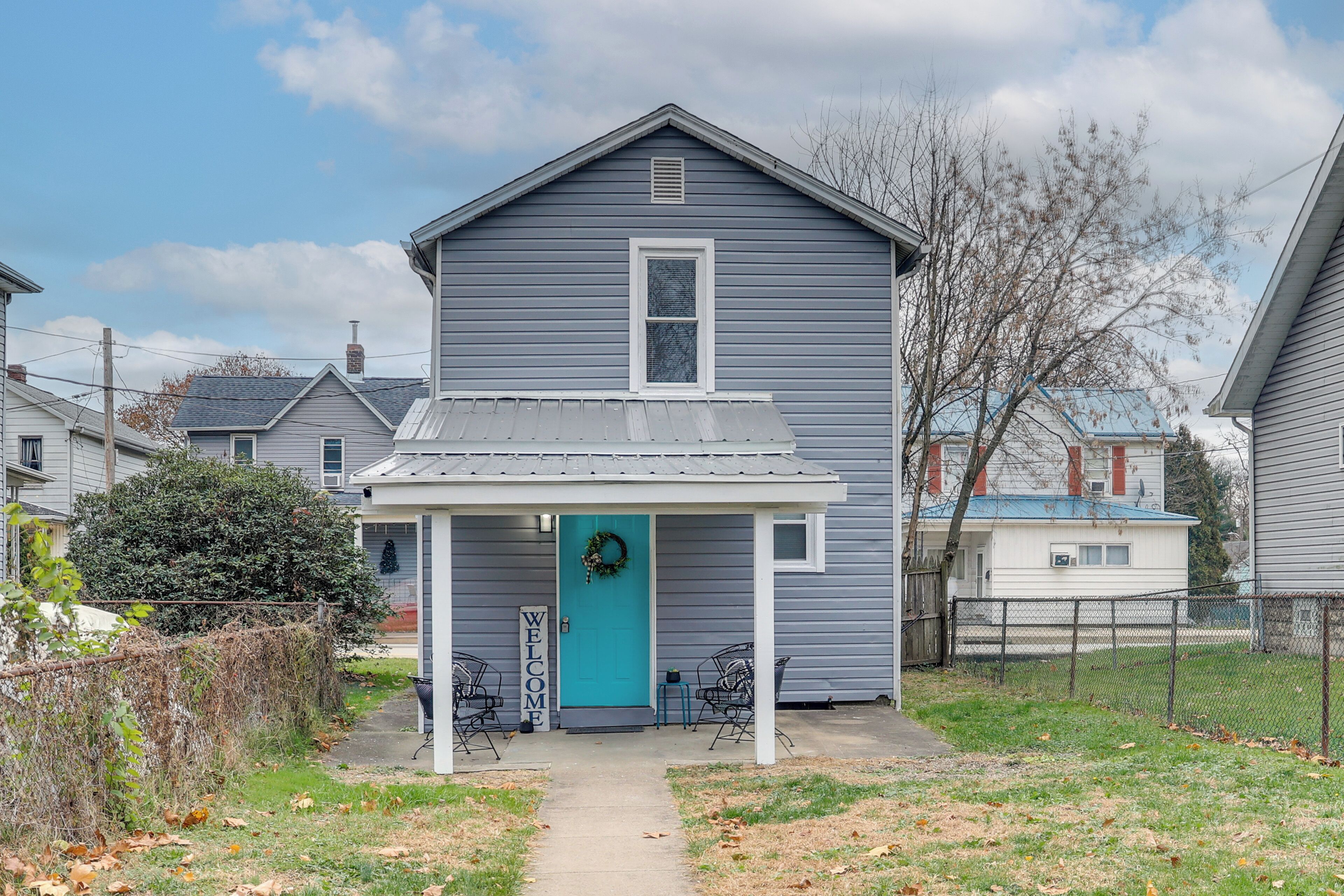 A two-story house with a blue front door, a porch with two chairs, and a 'WELCOME' sign.