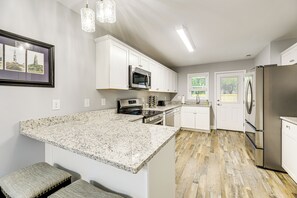 Cocina moderna con armarios blancos, encimeras de granito, electrodomésticos de acero inoxidable y suelo de madera.