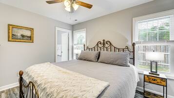 A bedroom with a bed, a ceiling fan, a nightstand, a window with blinds, and a framed picture on the wall.