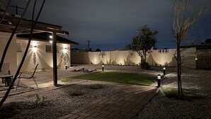 A well-lit patio area with a brick pathway, outdoor seating, and a wall with decorative patterns. - 4 bedrm, 8 Guest house in Central Phoenix WiFi, Putting Green, Mountain Preserve (Phoenix)