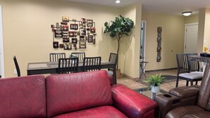 A living room with a red sofa, a brown leather chair, a dining table with chairs, a ceiling fan, and a wall with framed pictures. - 4 bedrm, 8 Guest house in Central Phoenix WiFi, Putting Green, Mountain Preserve (Phoenix)