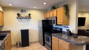 A compact kitchen with wooden cabinets, a stainless steel refrigerator, a microwave, an oven, and a granite countertop. - 4 bedrm, 8 Guest house in Central Phoenix WiFi, Putting Green, Mountain Preserve (Phoenix)