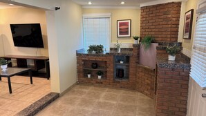 A compact living space with a TV, seating area, and a brick accent wall. - 4 bedrm, 8 Guest house in Central Phoenix WiFi, Putting Green, Mountain Preserve (Phoenix)