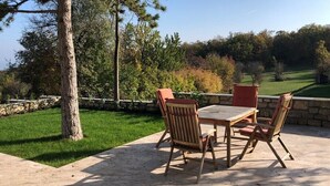 An outdoor patio with a wooden table and four chairs, surrounded by a stone wall and a view of a golf course.