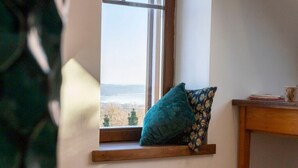 A window with a view of a landscape, a wooden shelf with a cushion, and a small table with a book.
