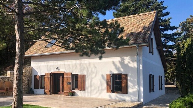 A white building with a tiled roof, wooden shutters, and a stone wall.