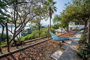 A hammock on a stone pathway with a view of a lake and trees.