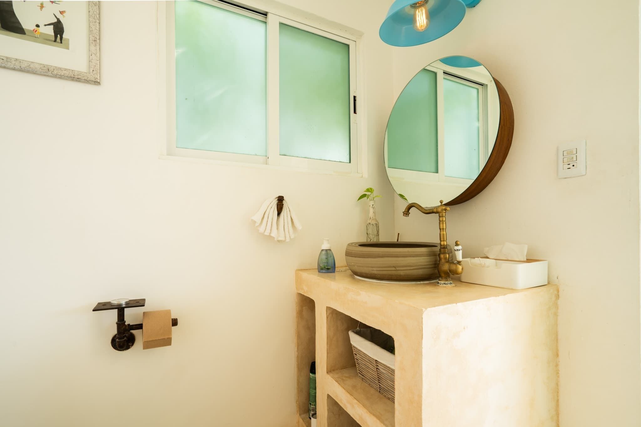 A bathroom with a round mirror, a sink with a bowl, a towel rack, and a window with frosted glass.