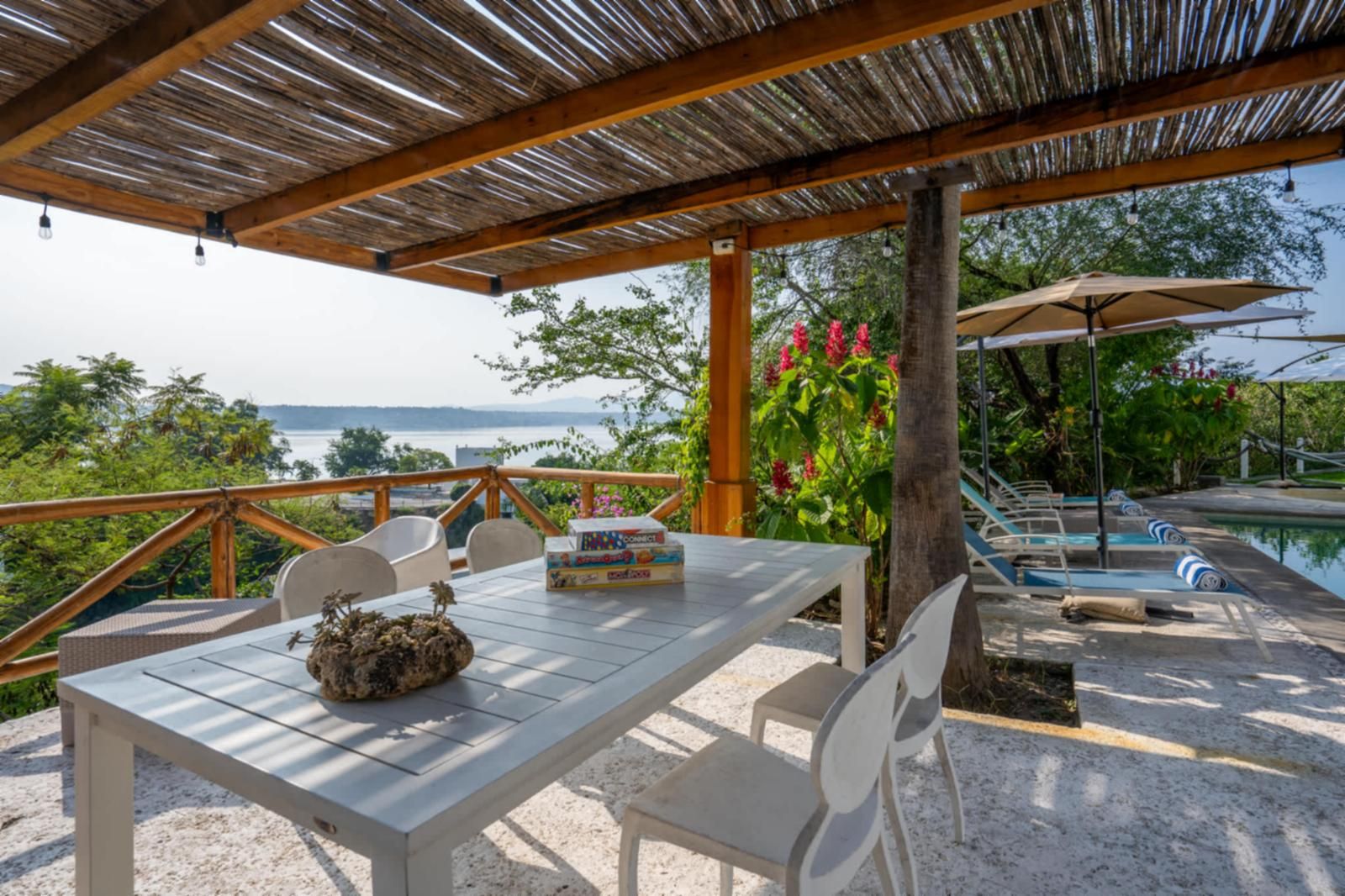 Ein überdachter Außenbereich mit Tisch und Stühlen, einem Pool und Blick aufs Meer.