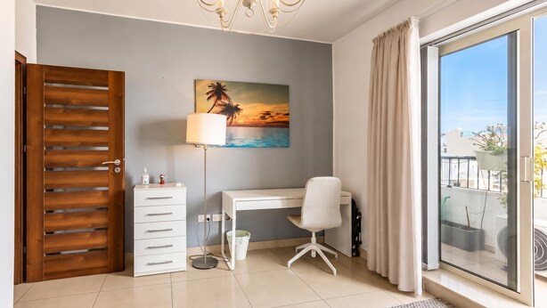A room with a desk, chair, chandelier, painting, and a sliding glass door to a balcony. - Modern and Comfortable Apart Savoy Garden (Gzira)