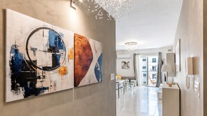 A modern hallway with abstract wall art, a chandelier, and a view into a dining area. - Modern and Comfortable Apart Savoy Garden (Gzira)