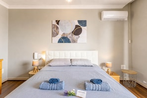A hotel room with a bed, two bedside tables with lamps, a wall-mounted air conditioner, and a painting. - Modern and Comfortable Apart Savoy Garden (Gzira)