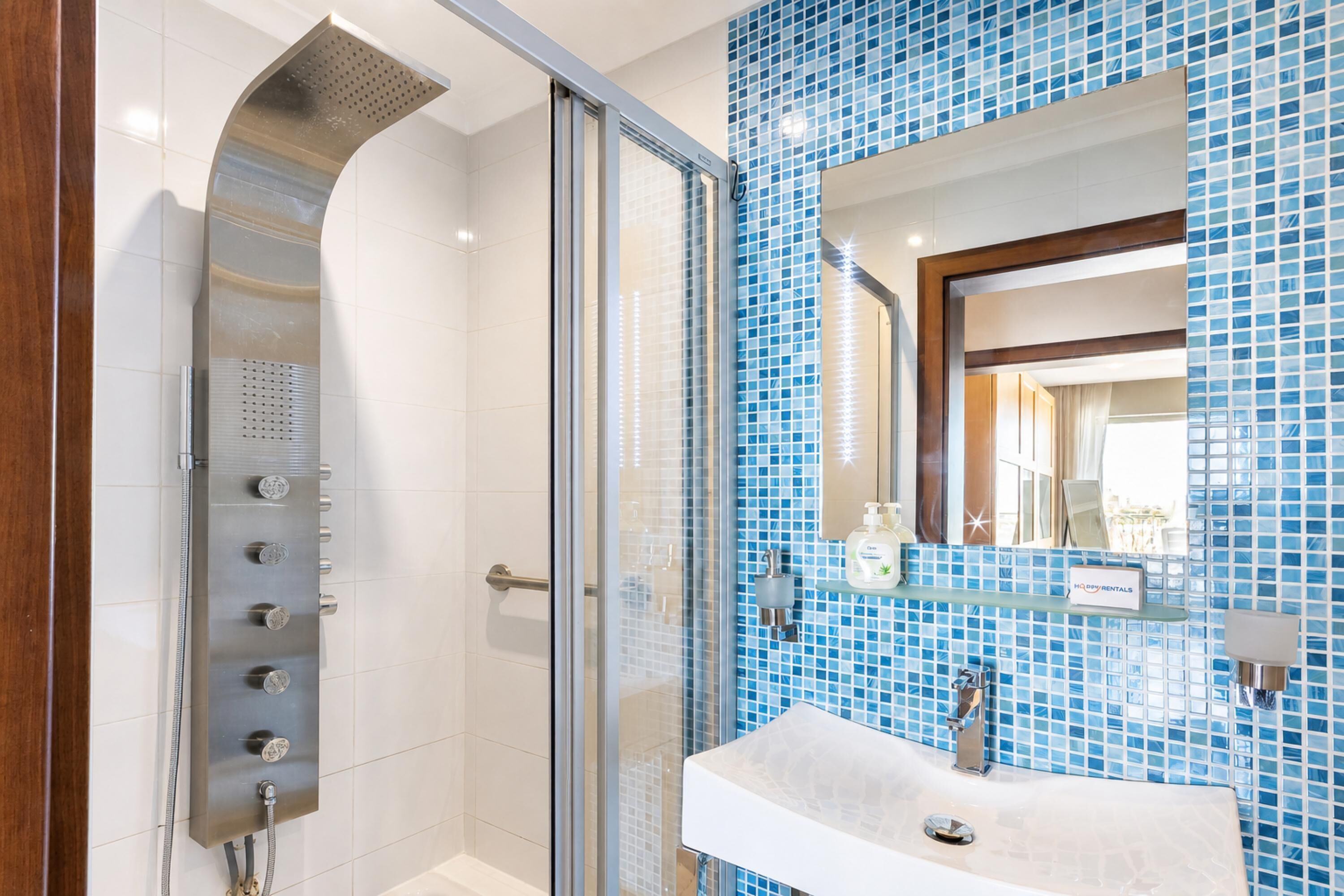 A modern bathroom with a glass shower enclosure, a white sink, and blue mosaic tiles.