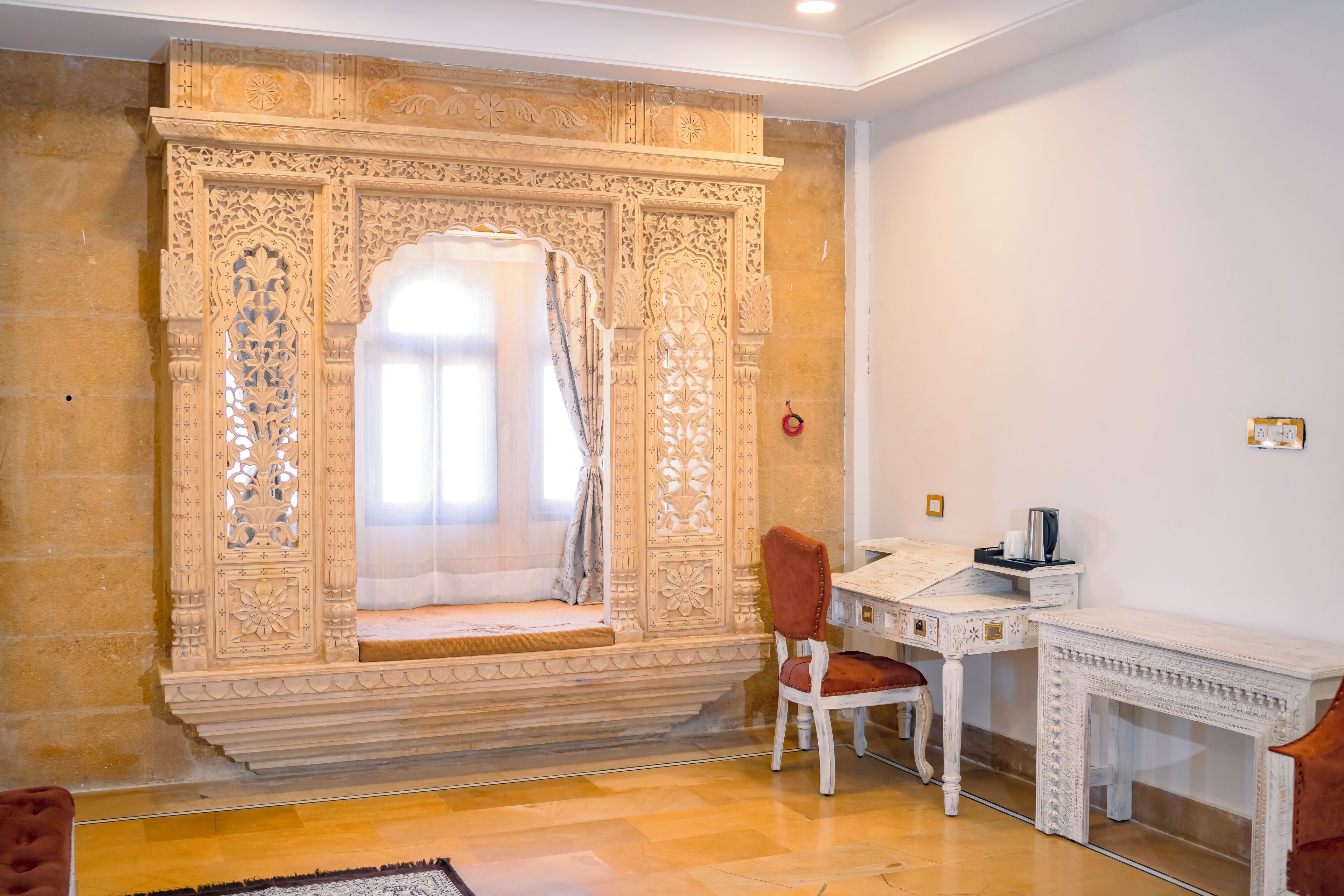 A room with a traditional carved wooden partition, a white desk with a chair, and a small table with a red chair.