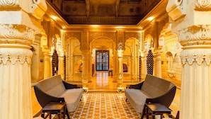A luxurious lobby with ornate columns, a checkered floor, and a grand staircase leading to a balcony. - Hotel Durjay Garh (Jaisalmer)