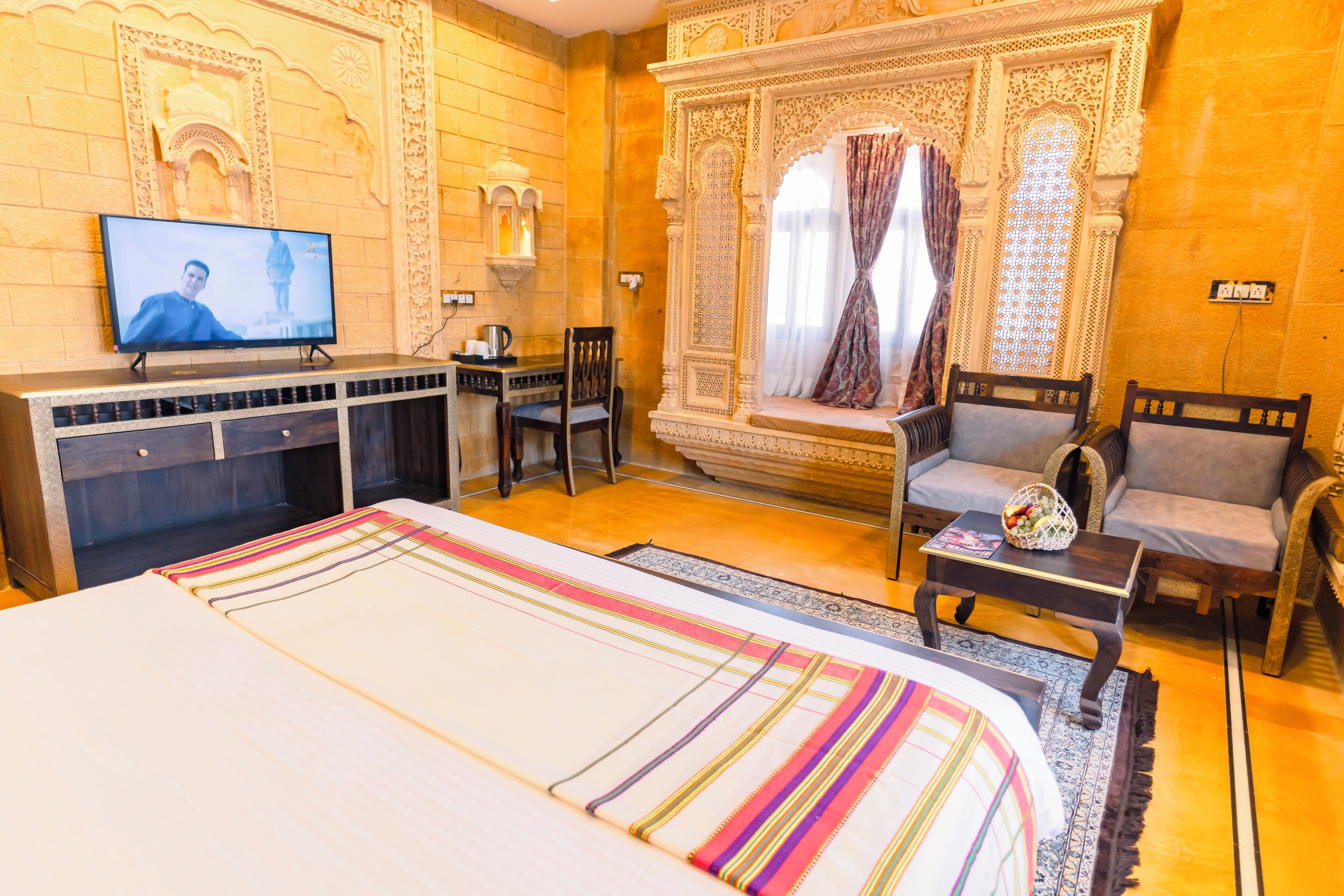 Una habitación de hotel con una cama, televisión, escritorio y dos sillas.