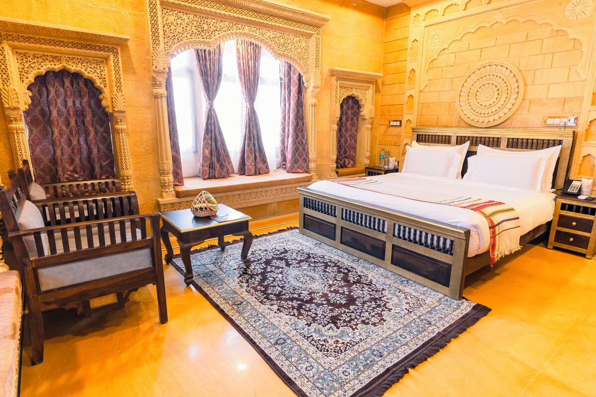 Une chambre traditionnelle comprenant un lit, un bureau et une chaise, agrémentée de motifs complexes sur les murs et d’un tapis à motifs.