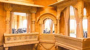 A room with ornate stone carvings, a seating area with chairs, and a view through an arched window. - Hotel Durjay Garh (Jaisalmer)