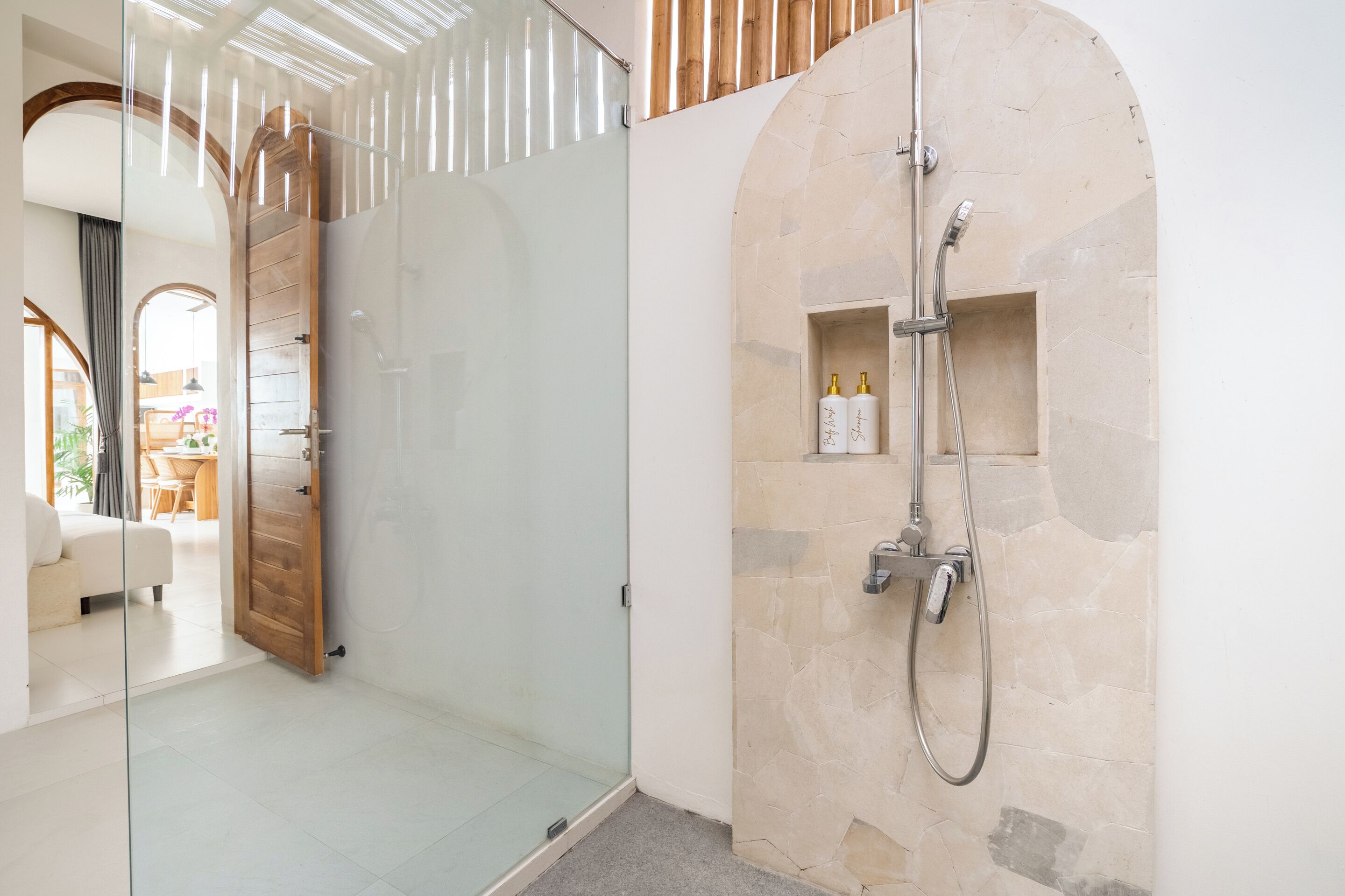 A modern bathroom with a glass-enclosed shower, a stone wall, and a wooden door.
