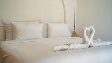 Una cama cuidadosamente arreglada con sábanas y almohadas blancas, una cesta tejida y una toalla doblada en forma de cisne.