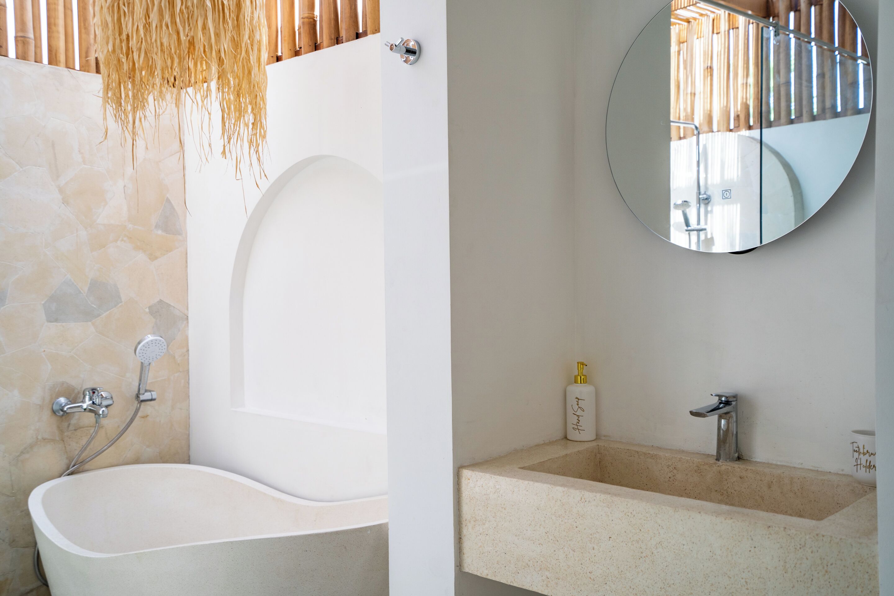 A bathroom with a freestanding bathtub, a round mirror, and a sink with a faucet.