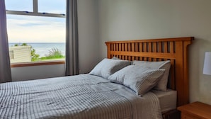 A bedroom with a wooden headboard, a bed with a striped quilt, and a view of the sea through a window.