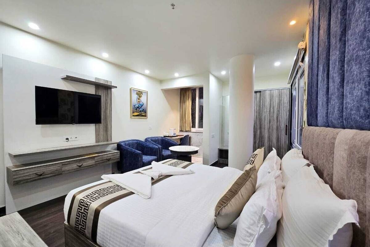 A hotel room with a large bed, a TV mounted on the wall, a seating area with chairs, and a small table.