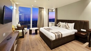 Habitación de hotel moderna con una cama grande, televisión, balcón con vistas a la ciudad y suelo de madera.