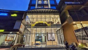 Entrada de un hotel con fachada de vidrio, una recepción y una escalera que lleva al vestíbulo.