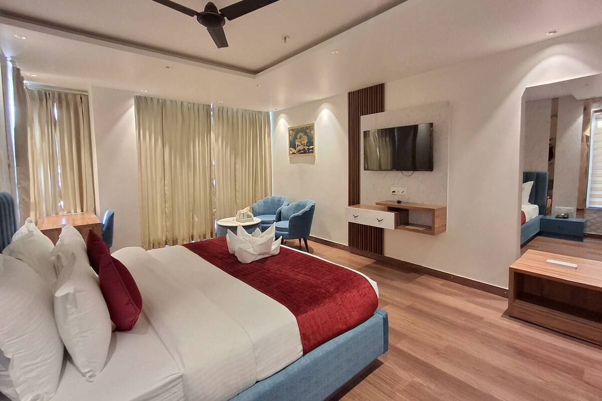 A modern hotel room with a large bed, a desk, a TV, and a ceiling fan.