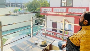 Un hombre sentado en un balcón con vistas a un edificio y montañas al fondo.