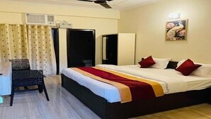 Una habitación de hotel con una cama, un escritorio, una silla, un ventilador de techo y un cuadro en la pared.