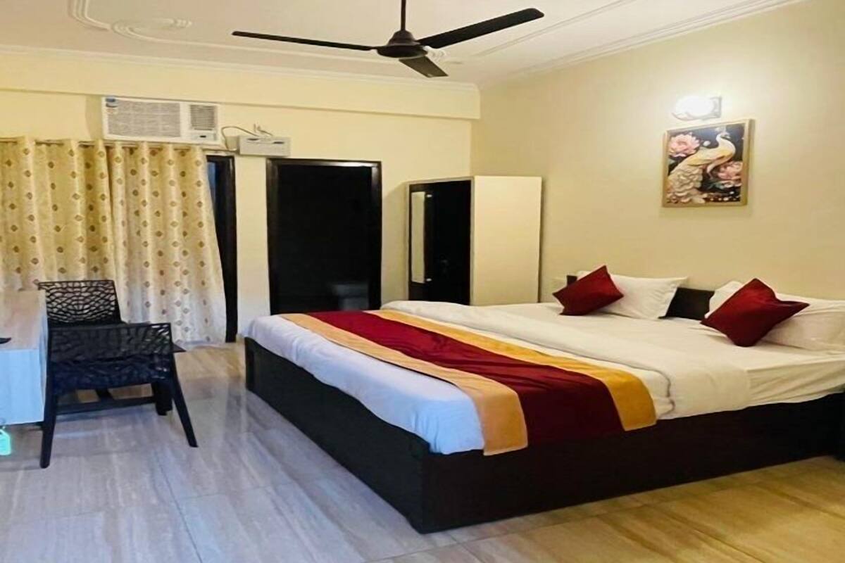 A hotel room with a bed, a desk, a chair, a ceiling fan, and a painting on the wall.