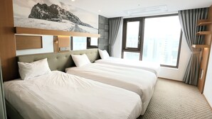 A hotel room with two beds, a large window with curtains, a mounted artwork of a mountain landscape, and a ceiling light.