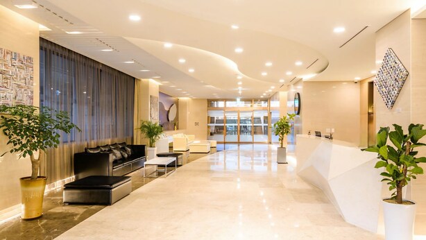 A modern hotel lobby with a reception desk, seating area, and potted plants.