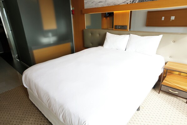 A hotel room with a large bed, a wooden nightstand, a marble wall, and a mirror above the bed. - Asia Hotel Jeju (Jeju City)