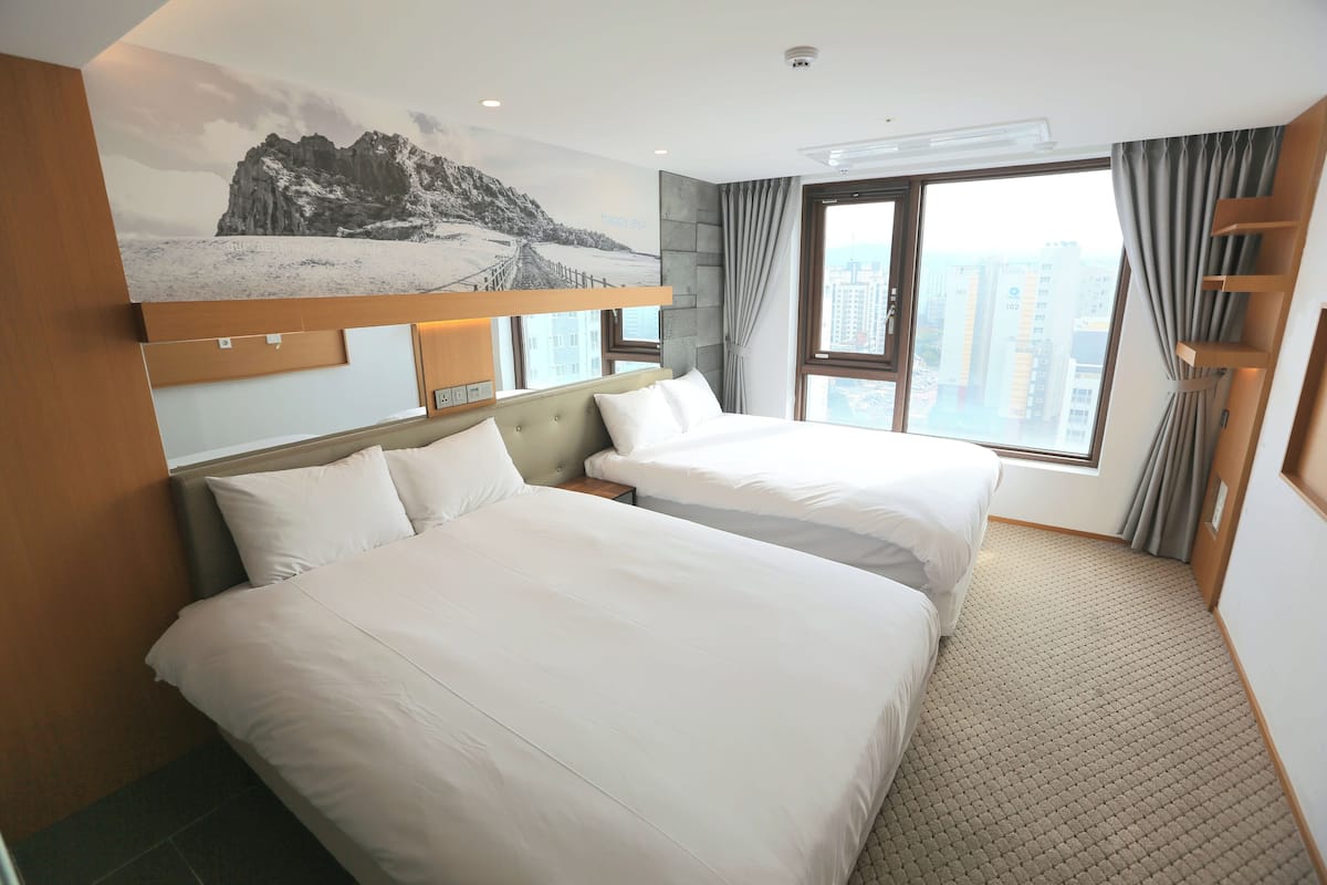 Een hotelkamer met twee bedden, een groot raam met uitzicht op de stad, een bergdecoratie aan de muur en een modern design.