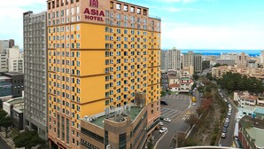 A multi-story hotel with a yellow facade and a view of the cityscape and sea in the background.