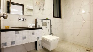 Un bagno con il water, un lavandino e una doccia. È presente un porta asciugamani e uno specchio sopra il lavandino.