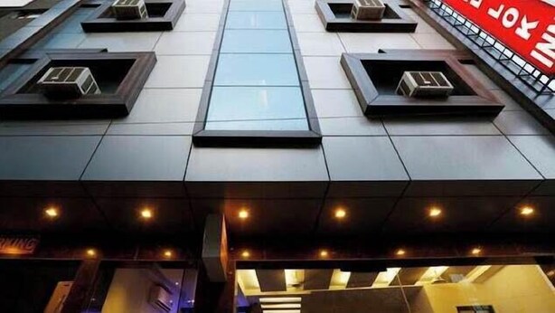 Un edificio moderno con facciata in vetro, condizionatori d'aria e un cartello ben visibile con la scritta 'PARKING'.