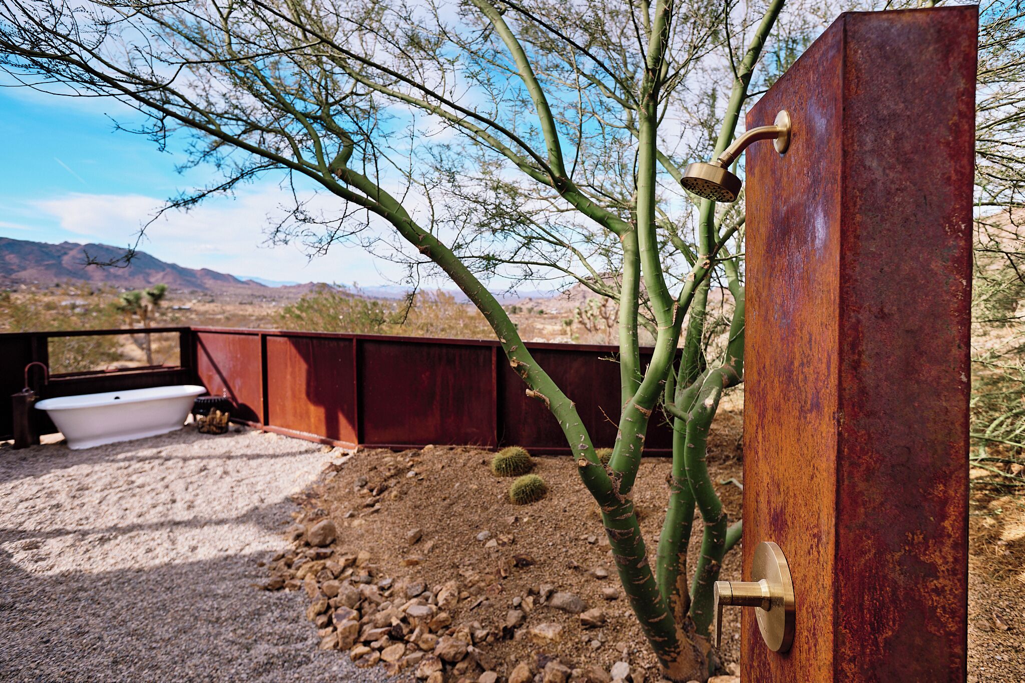 A rustic outdoor bathroom with a bathtub, a metal shower enclosure, and a cactus plant.
