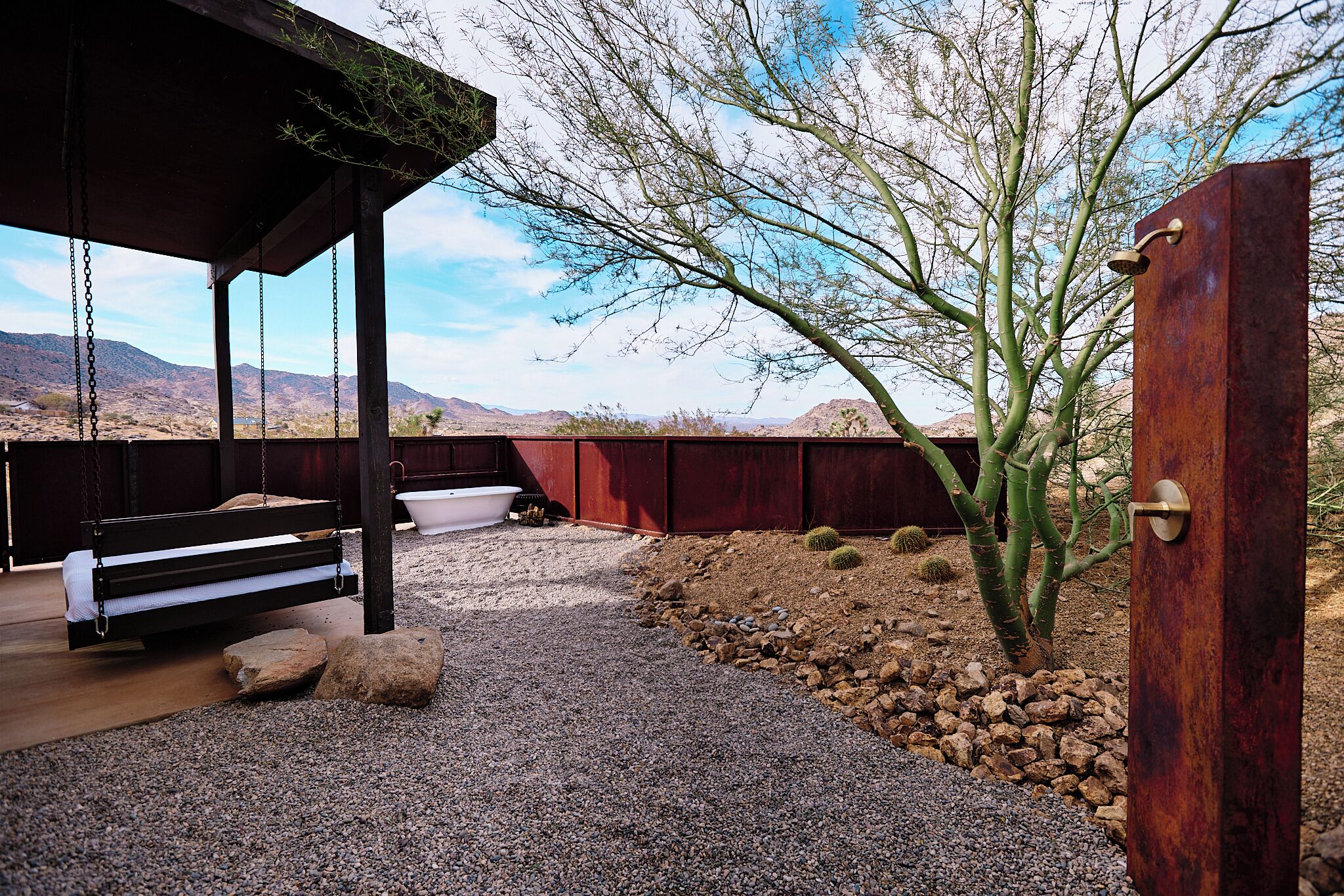 A wooden bench with a white cushion, a white bathtub, and a cactus in a desert landscape with mountains in the background.