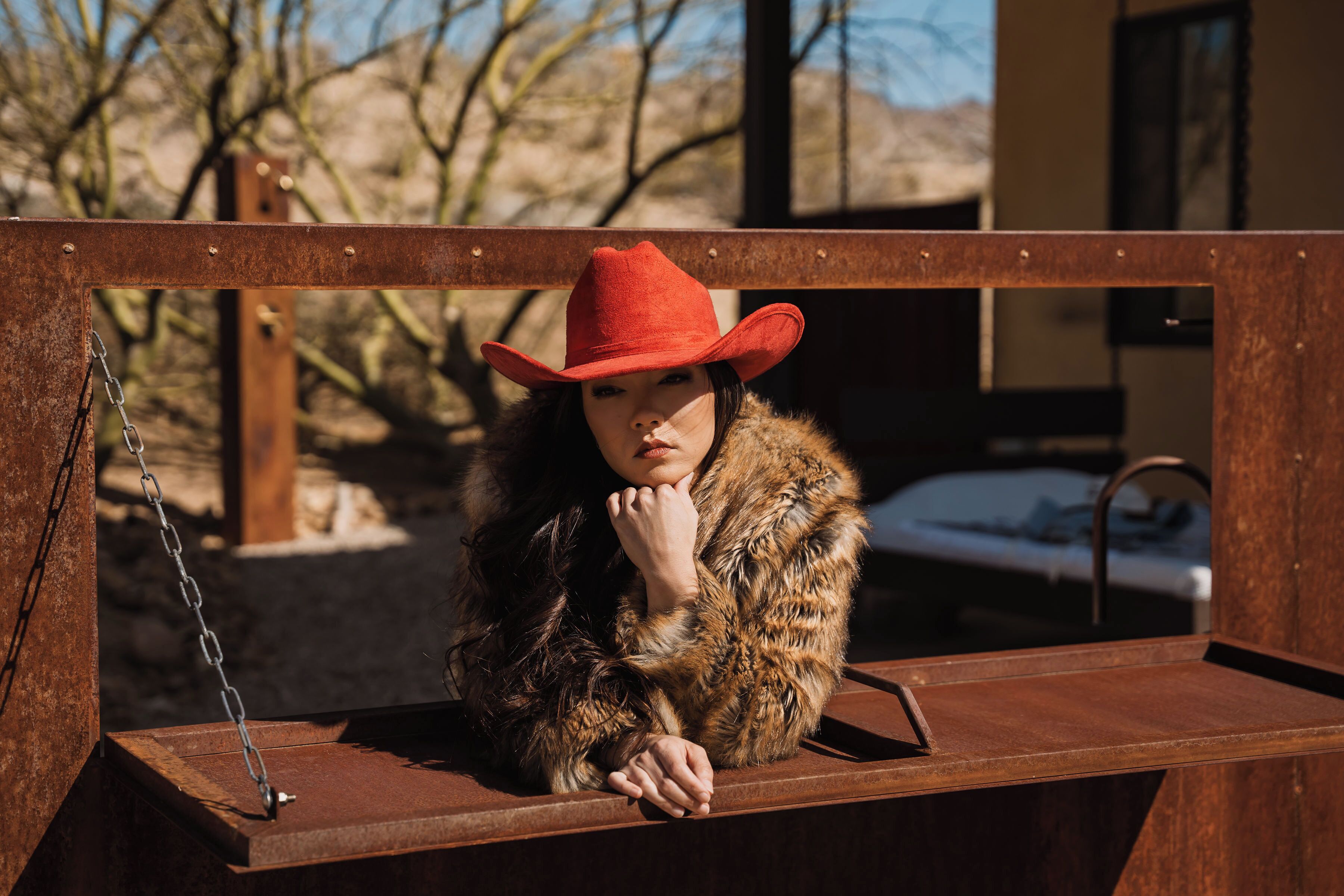 A person sitting on a bench with a chain link, wearing a red hat and a fur coat.
