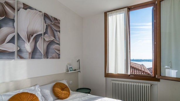 Un dormitori amb un llit, almoines, una finestra amb cortines, un radiador i una paret amb un motiu floral.
