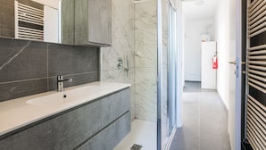 Un bany modern amb un lavabo de marbre, una dutxa i una zona de dutxa amb envàs de vidre.